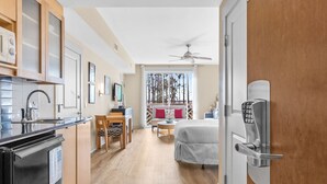 Une chambre d’hôtel compacte comprenant un coin cuisine, un lit, un bureau et un balcon avec vue sur les arbres.
