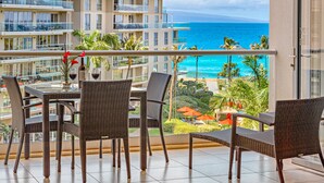 A balcony with wicker furniture, a glass table, and a bottle of wine. - Maui Resort Rentals: Honua Kai Hokulani 533 – Upgraded 5th Floor Oceanview Studio (Lahaina)