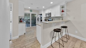 A modern kitchen with white cabinetry, a stainless steel microwave, and a built-in island with bar stools. - Golf Cart, Pet-friendly, Linkside Village 414 (Miramar Beach)