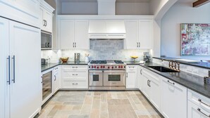 A modern kitchen with white cabinetry, a stainless steel range, and a large island with a black sink. - Sweeping Views and Exclusive Service in Luxurious Villas at Cortina Home (Mountain Village)