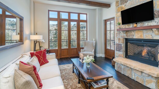 A living room with a stone fireplace, a large TV mounted on the wall, and a cozy seating area with a sofa and armchairs. - Sweeping Views and Exclusive Service in Luxurious Villas at Cortina Home (Mountain Village)