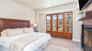 A bedroom with a large bed, a fireplace, and a view of mountains through French doors. - Sweeping Views and Exclusive Service in Luxurious Villas at Cortina Home (Mountain Village)