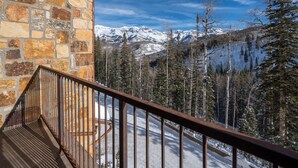 A stone wall and a metal railing overlooking a snowy mountain landscape with trees. - Sweeping Views and Exclusive Service in Luxurious Villas at Cortina Home (Mountain Village)