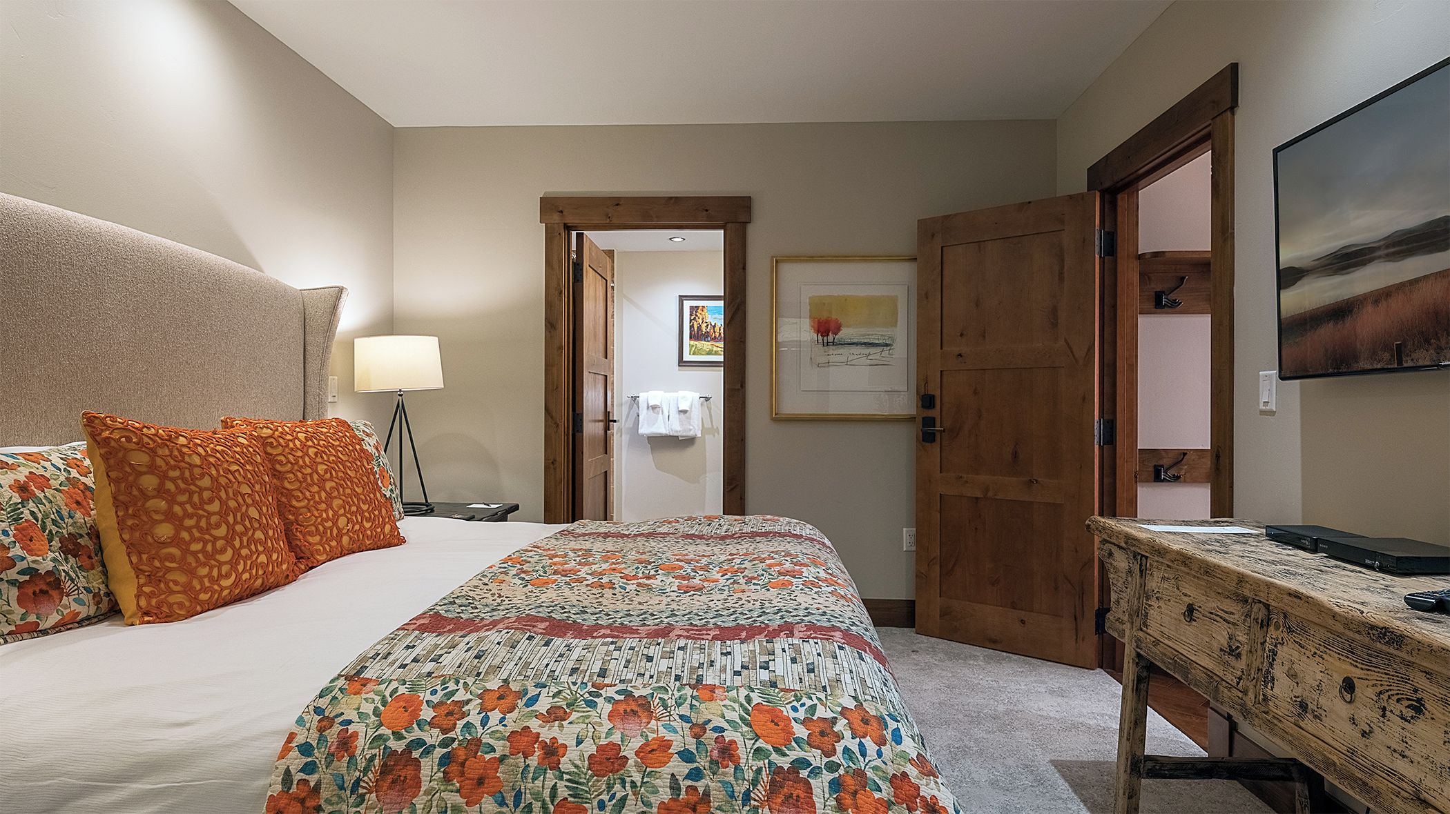 A hotel room with a bed, a desk, a lamp, and a painting on the wall.