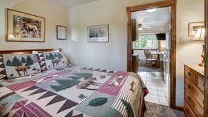 A bedroom with a large bed, a wooden headboard, a ceiling fan, and a door leading to a kitchen area.