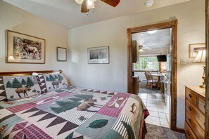 A bedroom with a large bed, a wooden headboard, a ceiling fan, and a door leading to a kitchen area.