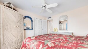 A bedroom with a bed, wardrobe, ceiling fan, and a mirror. - Kihei Beach #409 – Immersive Views and Tranquil Escape (Kihei, Maui)