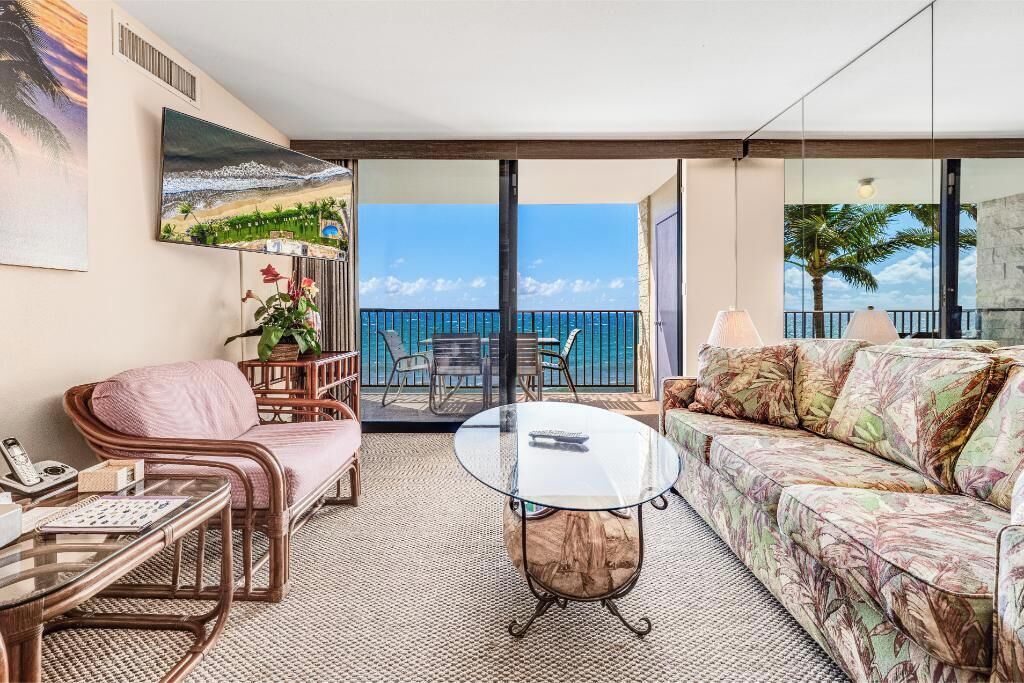 Ein Balkon mit Meerblick, möbliert mit Korbstühlen und einer Couch, sowie einem Glastisch.