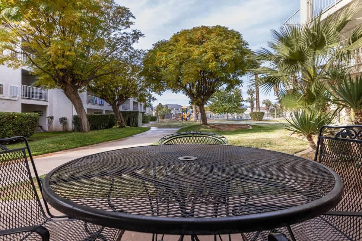A courtyard with a round metal table and chairs, surrounded by trees and a building.