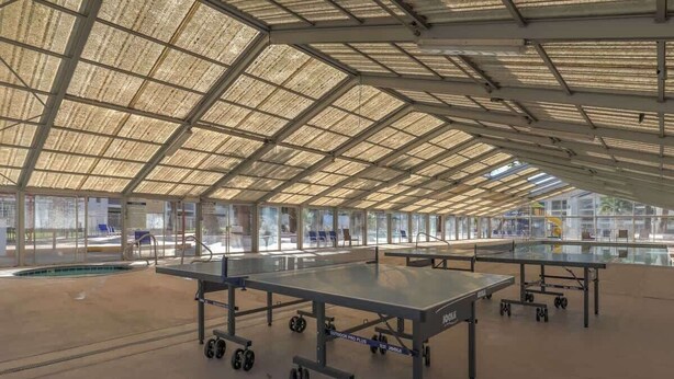 A spacious indoor area with a high ceiling and large windows, featuring multiple ping pong tables.