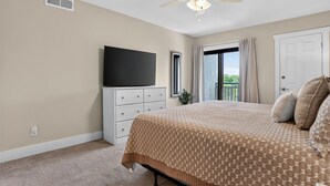 Een slaapkamer met een bed, een plafondventilator, een televisie, een raam en een deur.
