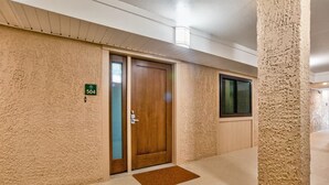 Een hotelgangen met een houten deur met het nummer 504, een deurmat en een raam aan de rechterkant.