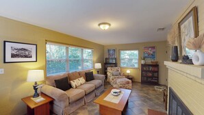 A living room with a beige sofa, two armchairs, a coffee table, and a fireplace. There are bookshelves, a lamp, and framed artwork on the walls. - Millican North - B 2 bedrooms, 2 bathrooms (Jekyll Island)