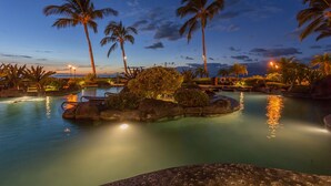 Ein Poolbereich eines Resorts bei Nacht, mit Palmen, klarem Himmel und ruhiger Wasseroberfläche.