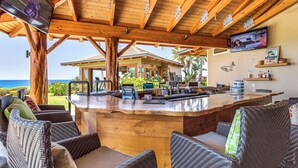 Ein Barbereich aus Holz mit Korbmöbeln, einem Fernseher und Blick auf den Ozean.