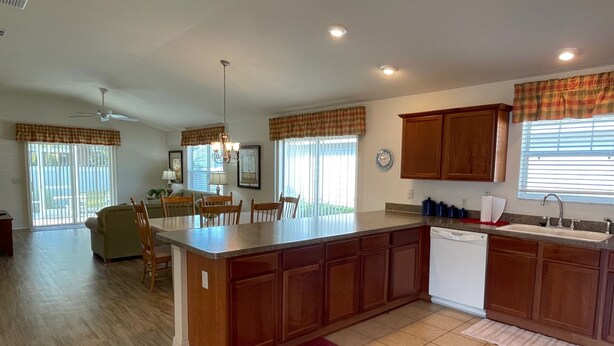 A spacious kitchen with a central island, wooden cabinets, and a dining area with chairs. - Walking distance to Lake Sumter Landing! Small Dog Friendly Villa w/Golf Cart (The Villages)