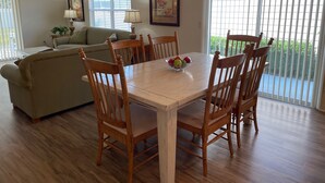 A dining area with a wooden table and chairs, a chandelier, and a window with blinds. - Walking distance to Lake Sumter Landing! Small Dog Friendly Villa w/Golf Cart (The Villages)