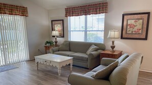 A living room with a sofa, a coffee table, and a lamp. - Walking distance to Lake Sumter Landing! Small Dog Friendly Villa w/Golf Cart (The Villages)