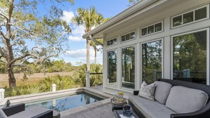 Área externa coberta com piscina, móveis de vime e grandes janelas com vista para uma paisagem natural.