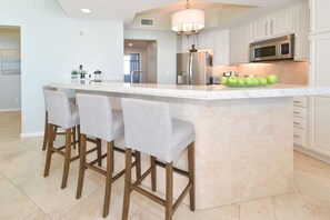 Una cocina moderna con una isla central, taburetes de bar, electrodomésticos de acero inoxidable y una lámpara colgante.