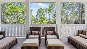 A covered outdoor seating area with wicker furniture and white railings, overlooking a forested area.