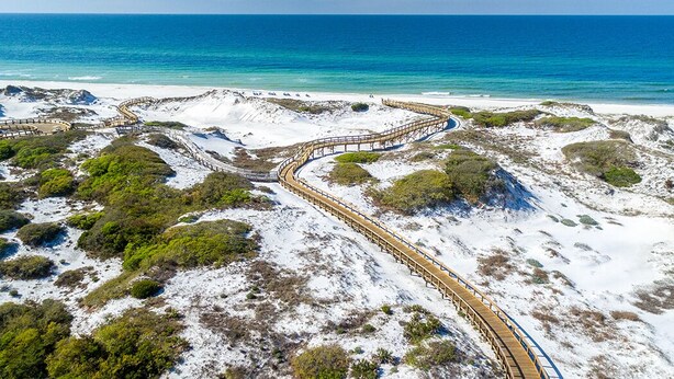 A coastal landscape with a winding wooden boardwalk leading to the beach.