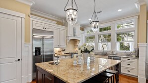 A spacious kitchen with a large island, stainless steel appliances, and a view through large windows.