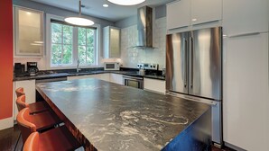A modern kitchen with a large island, stainless steel appliances, and a view of greenery outside. - 5 Heron- Great Family Retreat. 363 Yard walk to the Beach! (Hilton Head Island)