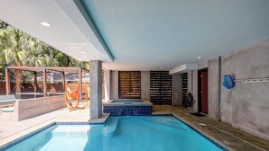 A modern indoor pool with clear blue water, a wooden deck area, and a covered seating area with a hammock. - 5 Heron- Great Family Retreat. 363 Yard walk to the Beach! (Hilton Head Island)