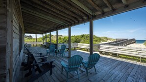 Een overdekt terras met houten banken en stoelen, met uitzicht op een strand en de oceaan.