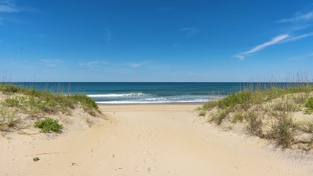 Een zandstrand met een helderblauwe lucht en oceaan.