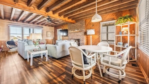 Een gezellige woonkamer met houten vloeren, een schouw met bakstenen en een witte eethoek.