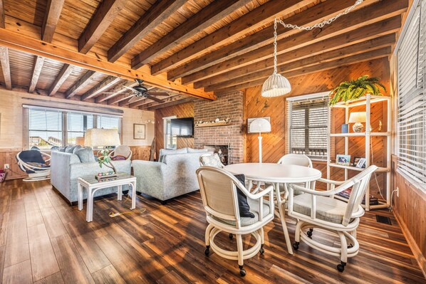 A cozy living room with wooden floors, a brick fireplace, and a white dining set.