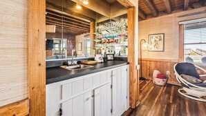 Een keuken met witte kasten, een zwart aanrecht en een houten plafond. Er is een hanglamp en een raam met zonwering.