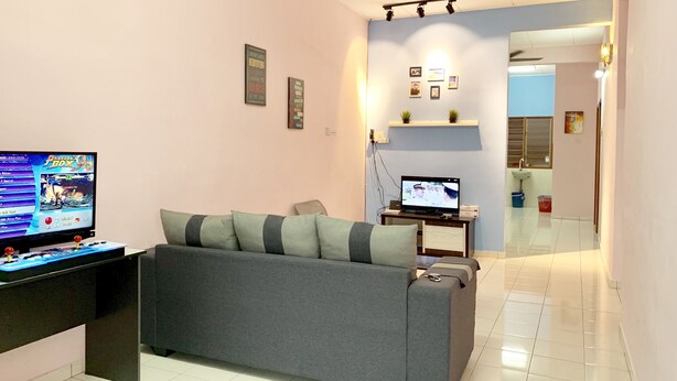 A living room with a grey sofa, a TV, a ceiling fan, and a small table with a laptop. - Sakura 2 Homestay Kampar (Kampar)