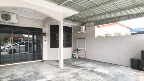 A covered parking area with a concrete floor, a red metal stand, and a white wall with a door. - Sakura 2 Homestay Kampar (Kampar)