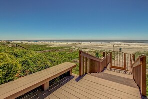 A wooden deck with a bench and a gate leading to a beach.