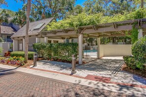 A covered outdoor area with a pool, surrounded by greenery and a paved walkway.