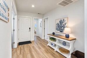 A hallway with wooden flooring, white doors, a bench with decorative items, and a wall-mounted artwork. - 8 Turtle Lane Club - Few Steps to the pool & beach! (Hilton Head Island)