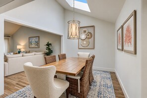 Een eetruimte met een houten tafel en rieten stoelen, een hanglamp en lijstwerken aan de wanden.