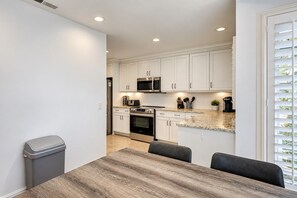 A modern kitchen with white cabinets, a microwave, oven, and a dining area with a table and chairs.