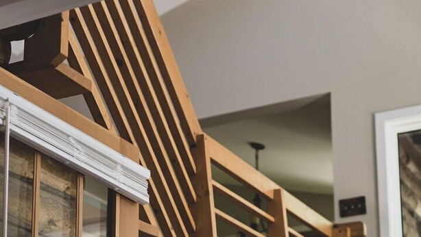 Una escalera de madera con una base de pared de piedra, una puerta de madera con paneles de vidrio y una ventana con persianas.