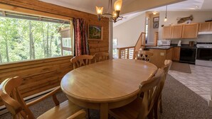Una mesa de comedor de madera con sillas, una cocina con armarios de madera y una escalera que lleva a un nivel superior.