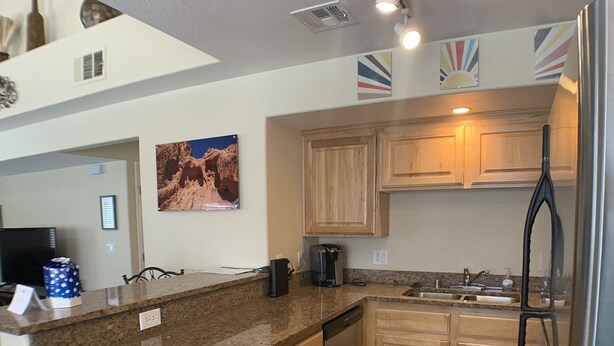 A modern kitchen with granite countertops, wooden cabinets, a stainless steel refrigerator, and a built-in dishwasher. - Home Field Advantage by Mesquite Vacation Rentals with Community Pool and $510 in free daily activities (Mesquite)