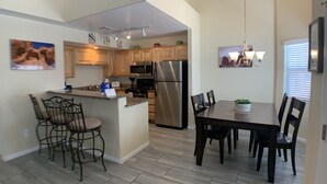 A modern kitchen with wooden cabinets, a stainless steel refrigerator, and a dining area with a table and chairs. - Home Field Advantage by Mesquite Vacation Rentals with Community Pool and $510 in free daily activities (Mesquite)