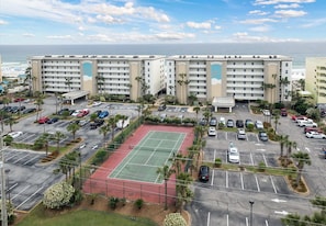 Um hotel com vários andares, quadra de tênis e estacionamento com diversos carros.
