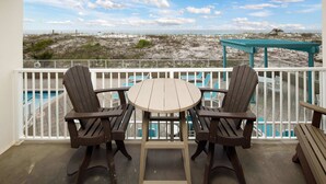 A balcony with a view of the beach, a wooden table, and two Adirondack chairs.