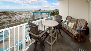 A balcony with a view of the beach, a wooden bench, and a table with chairs.