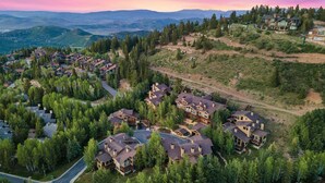 Un quartiere residenziale con diverse case circondate da alberi, una strada tortuosa e un paesaggio collinare sullo sfondo.