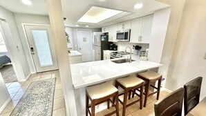 A modern kitchen with white cabinets, a large island with stools, a microwave, and a refrigerator.